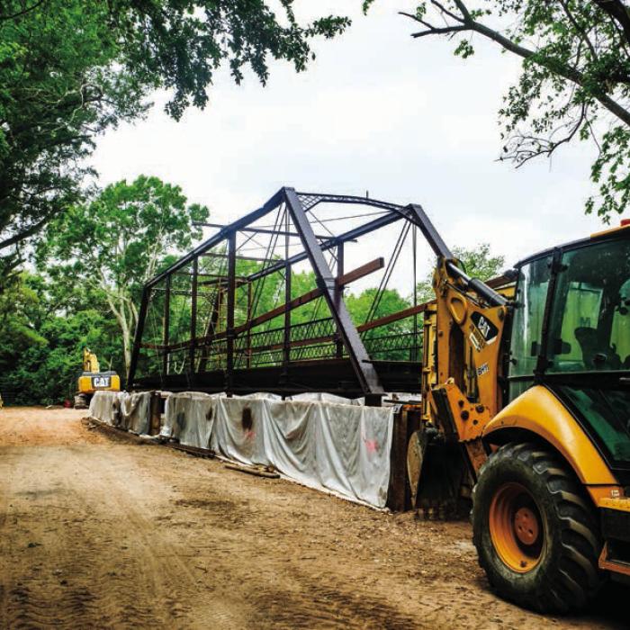 The Willow Springs Bridge currently sits on the south bank of Cummins Creek while contractors build new concrete approaches. Pct. 2 Commissioner Luke Sternadel said it took a 100-ton crane to pick up and move the bridge. The bridge itself does not weigh that much, but it took such a large piece of machinery due to the tricky nature of navigating the creek-bottom terrain.