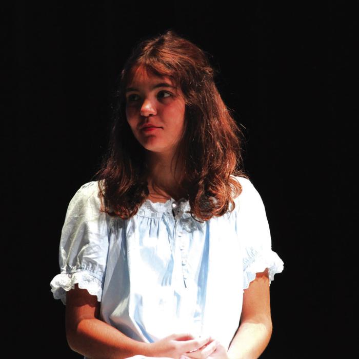 Carolina Lira, playing Wendy, sits atop a prop bed, waiting for instructions from Melissa Weltner.