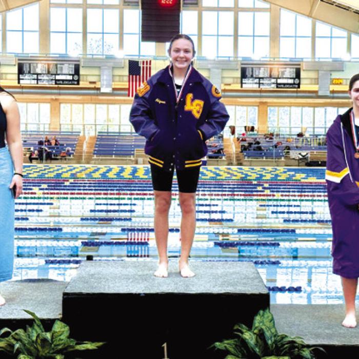 Adysen Janacek, center, and Makenna Emmel, right, stand atop the podium after medaling in the 100 freestyle. Janacek was the district champion.
