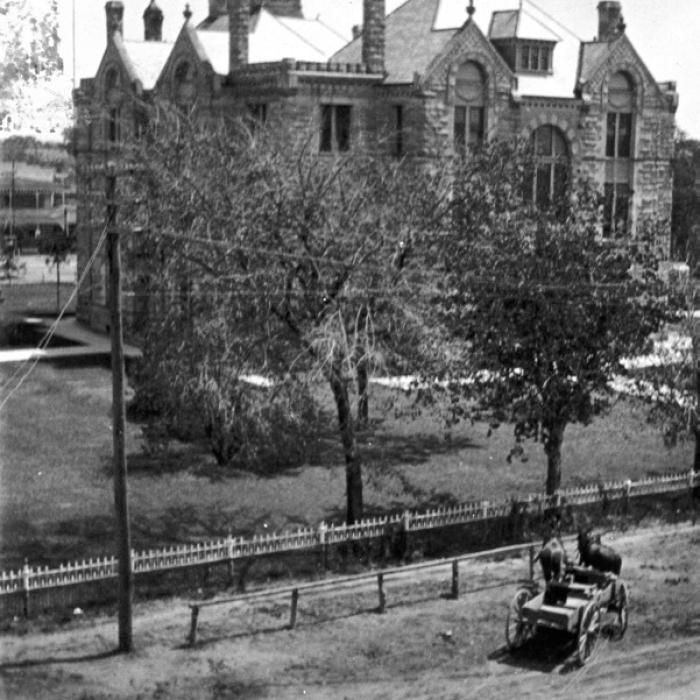 Circa 1900 photo of the west side of the courthouse taken from the second floor or roof of the Fink Building at 155 N. Main shows the iron fence that once surrounded the courthouse. A wagon drawn by a team of mules is tied to a hitching post, while a man is riding a bicycle down Main Street, which was still unpaved at the time. Photo courtesy of the Fayette Heritage Museum and Archives, La Grange.
