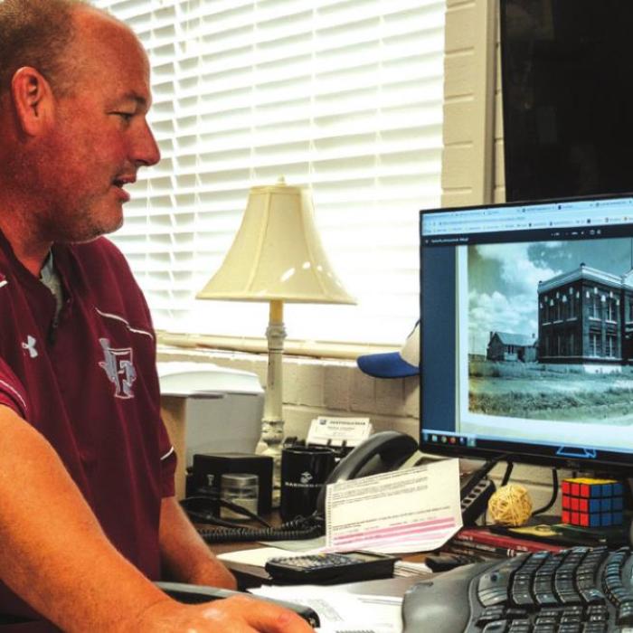 Fayetteville superintendent Dr. Jeff Harvey at his desk with an scanned image of the schoolhouse from 1944 on his computer screen. Photos by Andy Behlen
