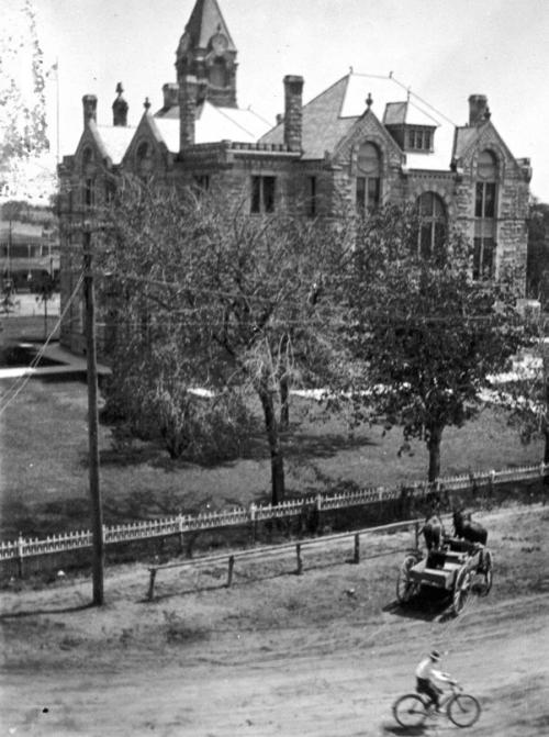 Circa 1900 photo of the west side of the courthouse taken from the second floor or roof of the Fink Building at 155 N. Main shows the iron fence that once surrounded the courthouse. A wagon drawn by a team of mules is tied to a hitching post, while a man is riding a bicycle down Main Street, which was still unpaved at the time. Photo courtesy of the Fayette Heritage Museum and Archives, La Grange.