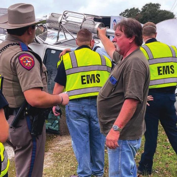 18-wheeler driver Jirrel Dean Warren of Seguin speaks with DPS Trooper Josh Berger Friday after a wreck, as county EMS officials respond to the scene. Warren took evasive action to avoid a wreck with another vehicle, but spilled his corn load. He was taken to St. Mark’s for evaluation. Photo by Andy Behlen