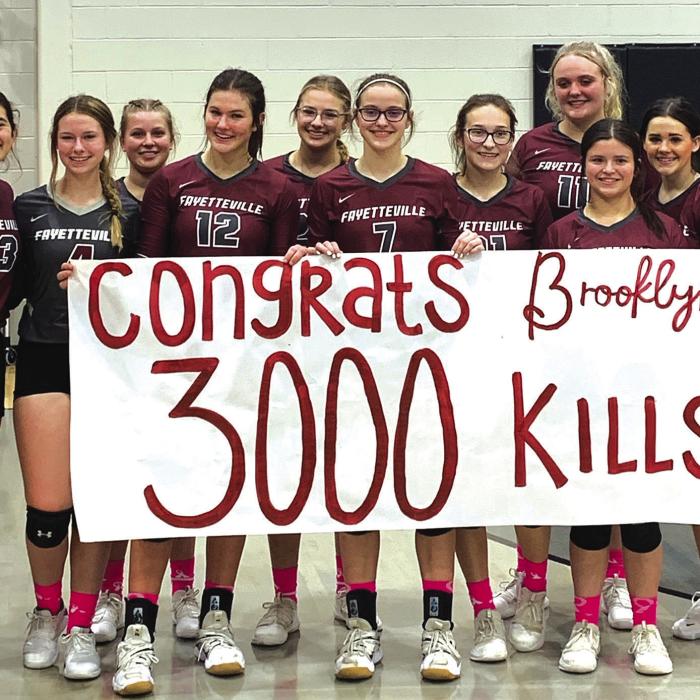 With her teammates and coaches joining her, Fayetteville’s Brooklyn Jaeger (seventh from left) holds up a banner congratulating her on reaching the milestone of 3,000 career kills after Friday’s match versus Mumford. Photo courtesy of Lisa Dyer