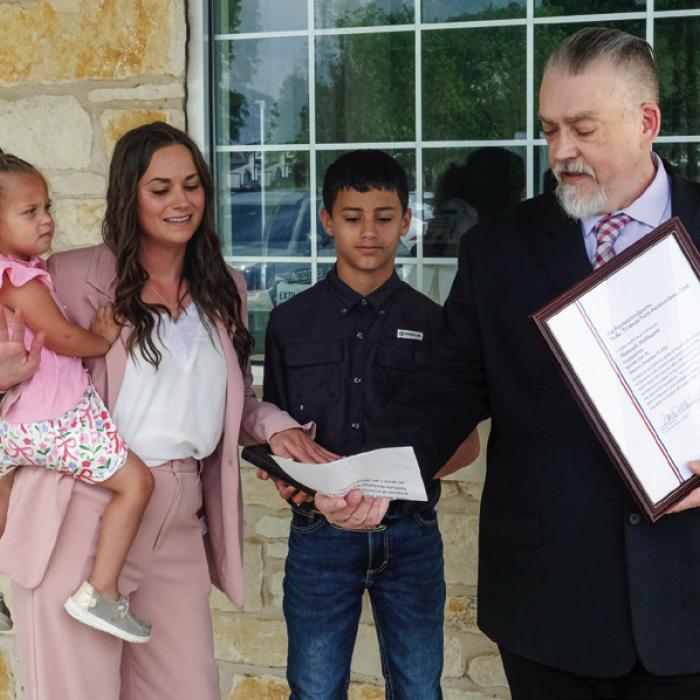 ce to the new Round Top Postmaster, Hannah Hollmann, on Friday, April 24. Also pictured are Hollmann’s children Ember and Evander. Pictured below are Hollmann and Biskner with several of Hollmann’s family members, colleagues and officials from the Town of Round Top. James Biskner (right), manager of post office operations for this region, delivers the oath of offi