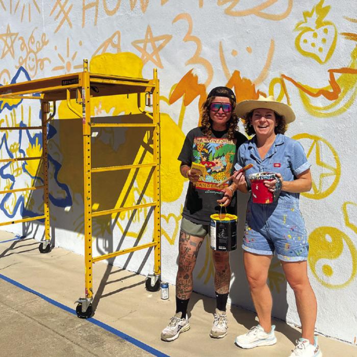 Artists Avery Houser, right, and Sullivan Meservey, left, in the early stages of their mural work on Main Street Monday. The artists’ process of “doodle grid” is shown. Those words and smaller pictures will not be part of the final design but are actually just a fun way to grid out their design on a larger surface without using either a ruler or a projector. Photo by Jeff Wick