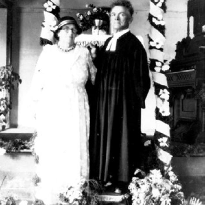 Minna and Rev. Carl Baer standing under a decorated arch in 1935, courtesy of the Fayette Heritage Museum and Archives.