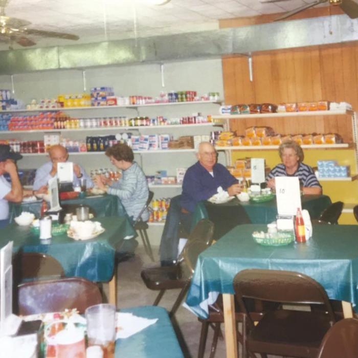 Left, a ribbon-cutting at the Warda Store, complete with a giant pair of scissors and, right, plenty of satisfied customers eating meals, with fully stocked grocery shelves behind them.