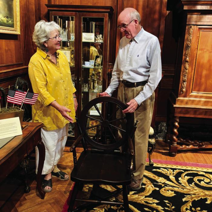 Lamar Lentz, Library and Museum Collections Curator, and Pat Johnson, Associate Curator, install the “Old Flax Spinning Wheel Chair,” an example of Colonial Revival folk art produced around the time of the 1876 Philadelphia Centennial, in the Round Top Festival Institute collection.