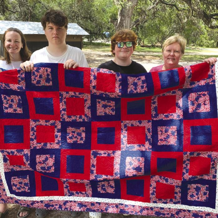 John Tajchman was presented a Quilt of Valor by his mother Marian. He served as a Sargent in the U.S. Army Intelligence from 2000-2004. John is on the right side of the quilt surrounded by his mother, sisters, and nephews. The quilt was made by the members of the Colorado Valley quilt Guild here in La Grange.