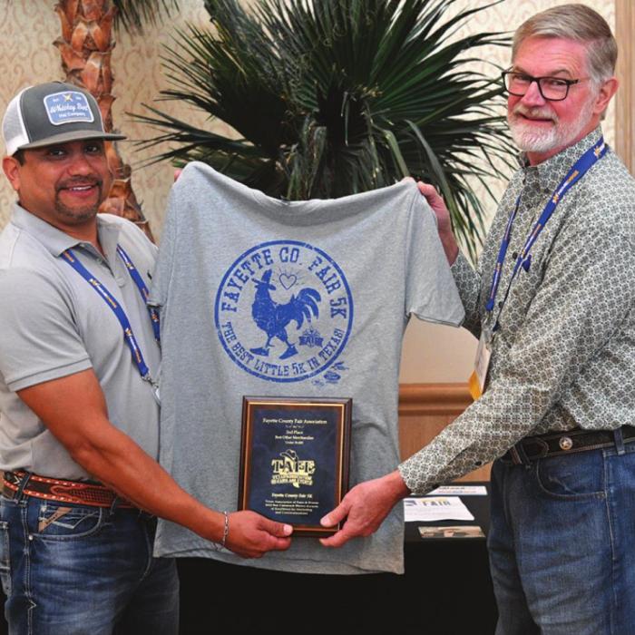 A T-Shirt was designed for the Fayette County Fair 5K Run that is organized by Aaron Muniz. The T-Shirt won second place in the Best Other Merchandise Category for 2021. The Association is very proud of this award. Pictured are Aaron Muniz and Michael Zuhn with the T-Shirt.