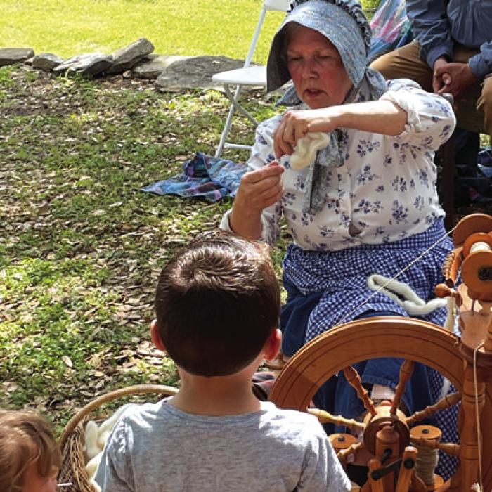 Volunteer Bobbie Nash demonstrates the use of a spinning wheel to kids at Monument Hill.