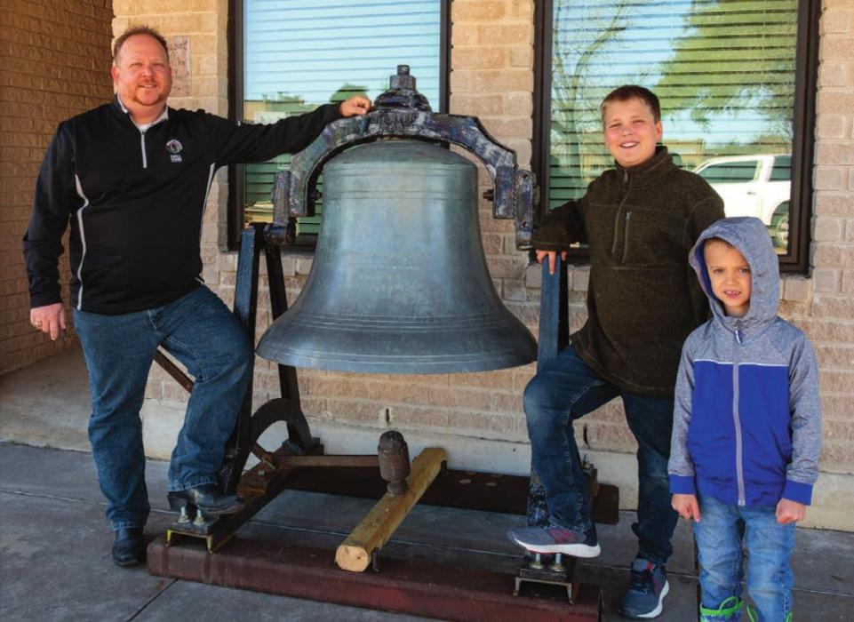 Erich Lehmann and his sons Daniel and Caleb stand next the bell Lehmann installed in front of his office on the Square in La Grange. Photo by Andy Behlen