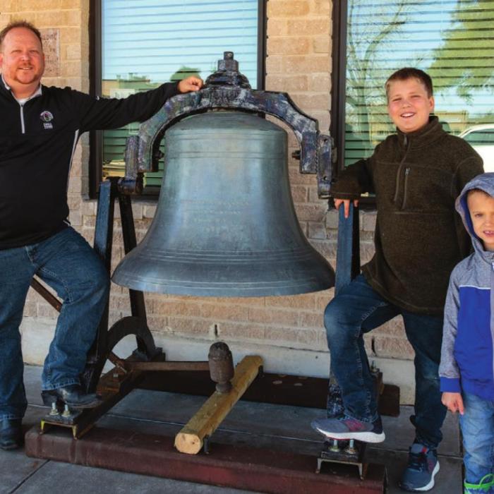 Erich Lehmann and his sons Daniel and Caleb stand next the bell Lehmann installed in front of his office on the Square in La Grange. Photo by Andy Behlen