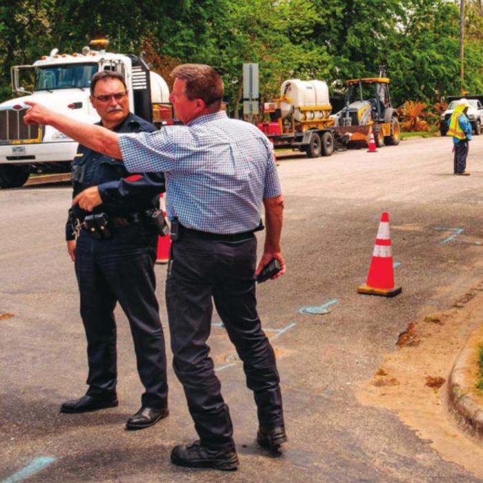Patrolman Curtis Zwahr and Sgt. Travis Anderson of the La Grange Police Department and La Grange Fire Chief Frank Menefee make plans to evacuate the neighborhood after a gas leak at the corner of Milam and Jackson streets Monday afternoon. A contract crew working for Centerpoint Energy (pictured in the background) accidentally struck a four-inch gas line while digging with an excavator. Photo by Andy Behlen