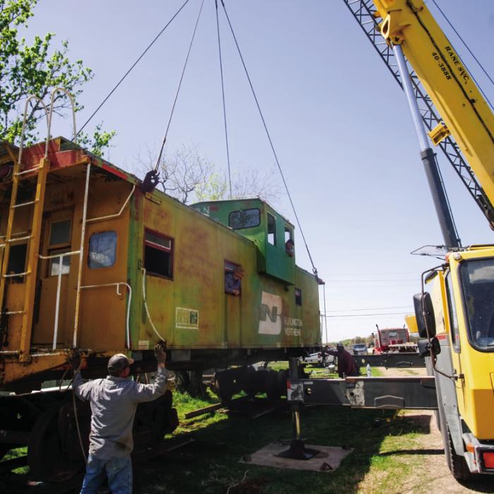 Charlie Brewer and Gary Gillentine peek out of the windows of this 1957 Burlington Northern Caboose as Ray’s Crane Service moves the caboose into place on wheels at Brewer’s home in La Grange near the intersection of Von Minden Road and Highway 71 on Wednesday. Brewer recently purchased the caboose and, with the help of Gillentine and Lee Kimbrell, is fixing it up as a tiny home to sell. More on the project in an upcoming edition of The Record. Photo by Andy Behlen