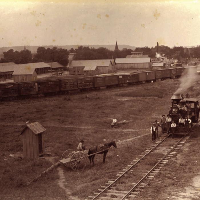 This Circa 1895 photograph of the M. K. &amp; T rail yard on the eastern end of La Grange (vicinity of 600 Block East La Fayette Street) looking south with the bluff off in the distance. Louis Melcher captured this view from the roof of the M. K. T. freight depot. Train cars, warehouses, elevated tanks and open sheds like those used by lumberyards are visible (present day Farmer’s Lumber Company).