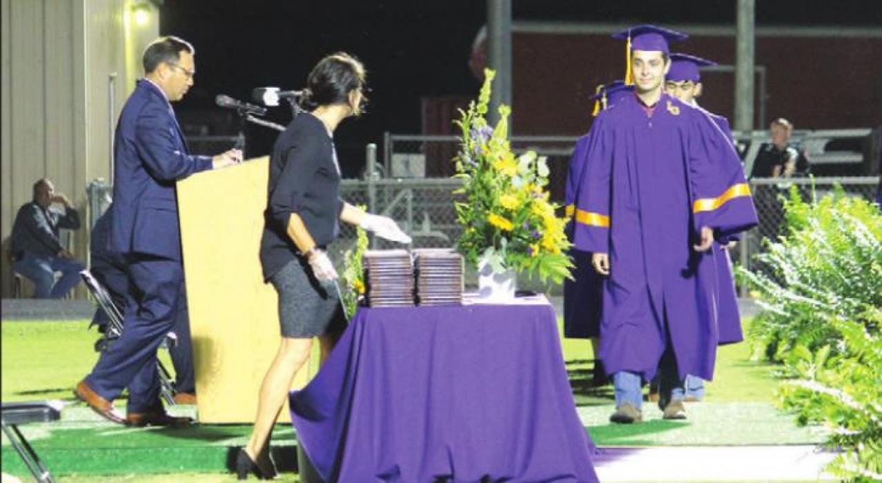Logan Adamcik, the first alphabetically to officially graduate, walks up to a table where every graduate grabbed their own diploma.