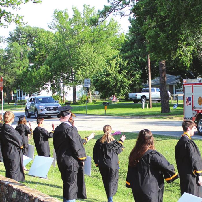Members of the Round Top-Carmine senior class watch and wave as nearly 100 vehicles, many decorated with signs, balloons, etc, rolled by the high school campus to cheer on the graduates. The event was organized to make up for some of the other senior events the class was going to miss out on because of coronavirus precautions. Photo by Jeff Wick