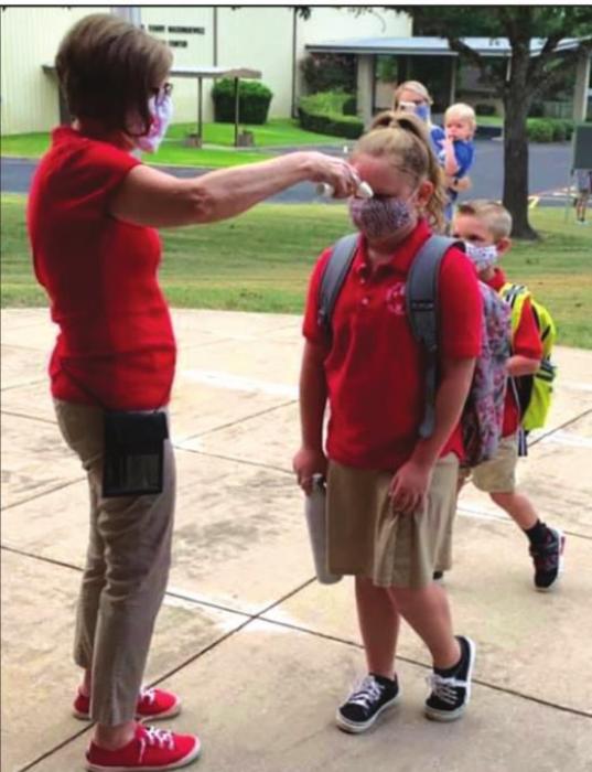 Sacred Heart School secretary Cindy Fletcher checks students’ temperatures as they walk in on the first day of school Thursday.