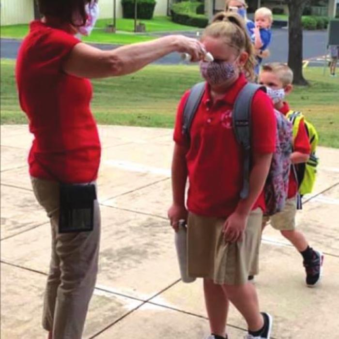 Sacred Heart School secretary Cindy Fletcher checks students’ temperatures as they walk in on the first day of school Thursday.