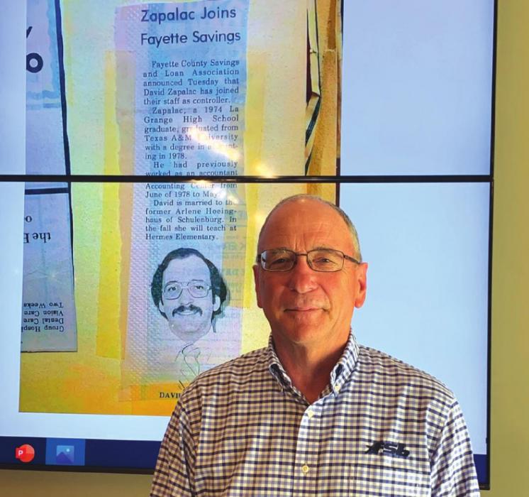 Fayette Savings Bank CEO David Zapalac stands next to a screen displaying an old newspaper article from 1981 announcing his hiring at the bank. Photo by Andy Behlen