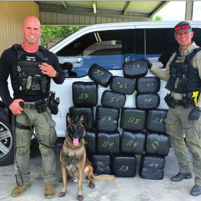 Left to right: Sgt. Randy Thumann, canine offi cer Kolt and Deputy David Smith stand next to their lates find, 182 pounds of marijuana.