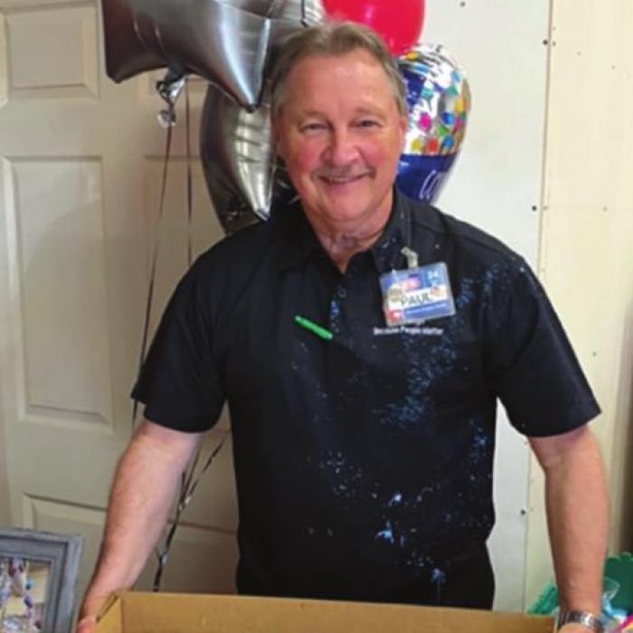 Paul Mikula poses with a cake at his retirement celebration Tuesday at HEB. His shirt is covered with remnants of a silly string spraying by his co-workers. Photo by Linda Morrison