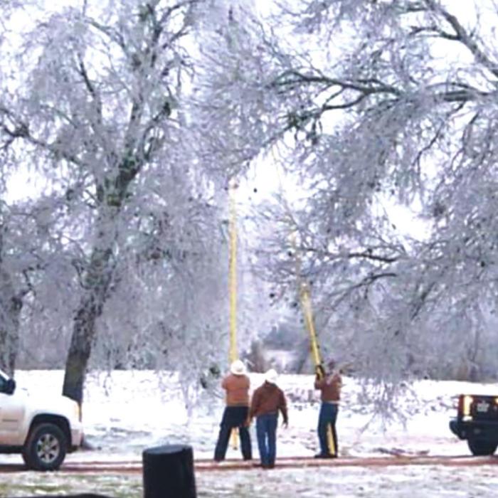 Trimming trees, heavy laden with ice that fell into a power line are Line Foreman Charles Srubar, Equipment Operator Ronnie Martinek, and Apprentice Lineman Macy Scott.