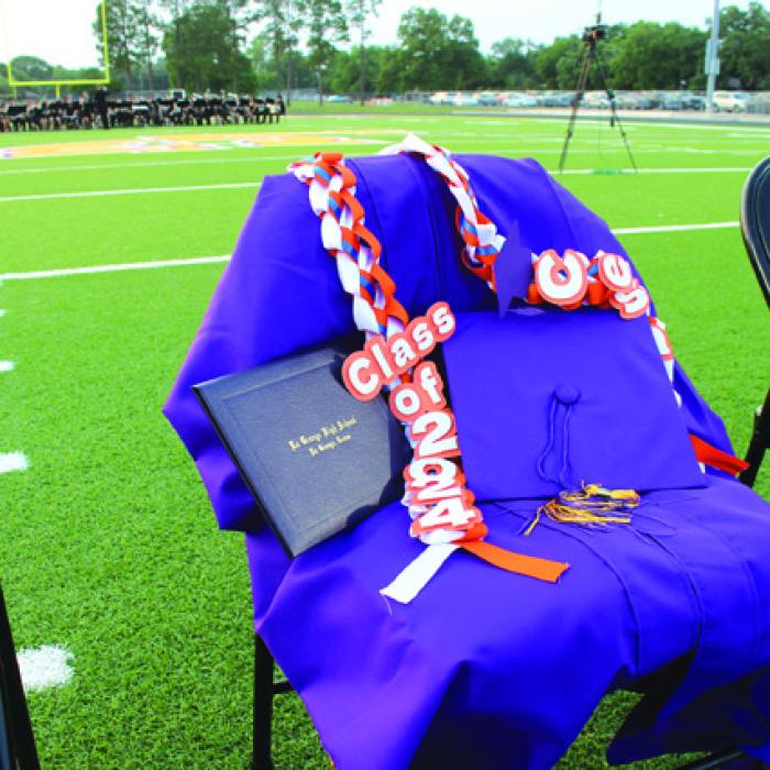 Above: An empty chair, draped with a gown and with his diploma, was left open among the seniors during Thursday’s graduation in honor of the late Cesar Villasana. He was a member of this class who died in 2022 after a long battle with leukemia. Right: Two seniors embrace Thursday. Photos by Jeff Wick