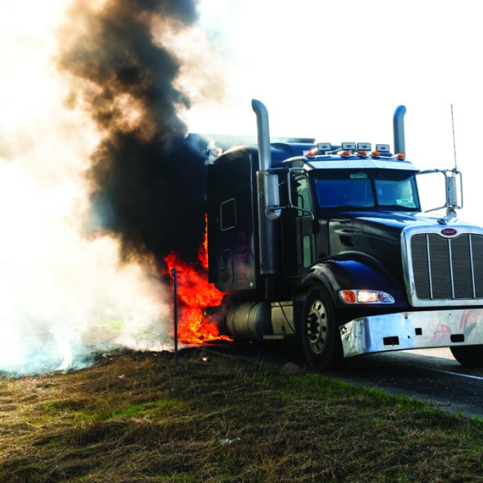 Above, a Peterbilt truck pulling a piece of oilfield equipment caught fire after a tire blow out on SH 71 at the Whataburger exit in La Grange Wednesday morning. Below, La Grange Fire Chief Frank Menefee sprays down the smoking rear axle where the fire started. Photos by Andy Behlen