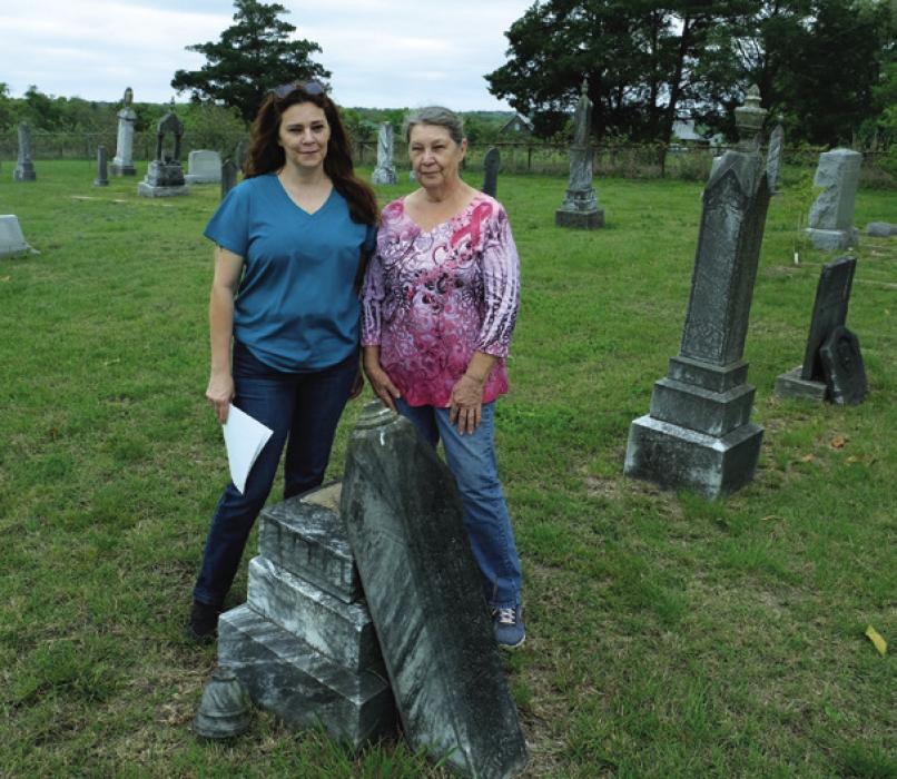 Shan Jakobeit, left, and her mother Connie stand by the grave of Caroline Otto, who died in 1898. The top of the gravestone has broken away from the leaning pedestal. Photo by Andy Behlen