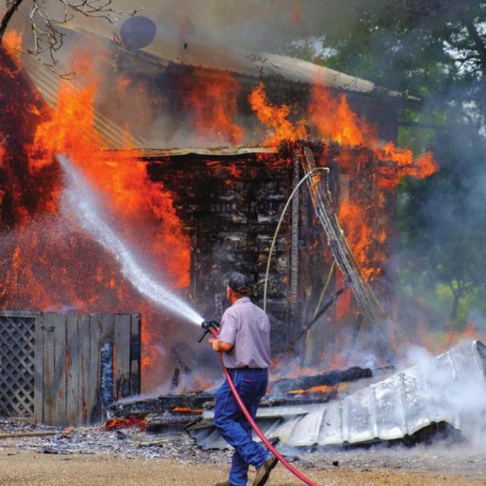 Schulenburg Firefighter Paul Zapalac, one of the first on scene, attacks a wall of burning cedar shingle siding.