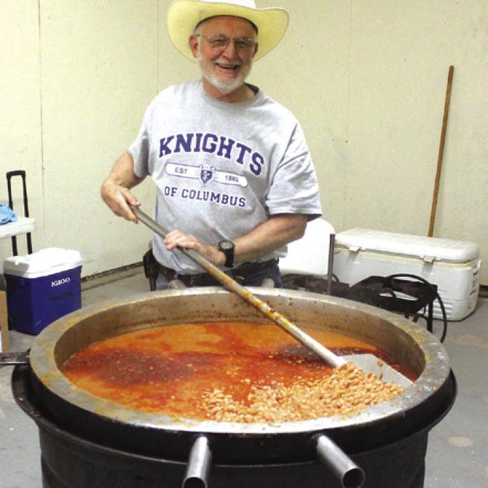 Jim Kothmann stirs up a massive kettle of 120 pounds of beans the Knights of Columbus prepared as part of the cyclists’ supper Saturday at the fairgrounds.