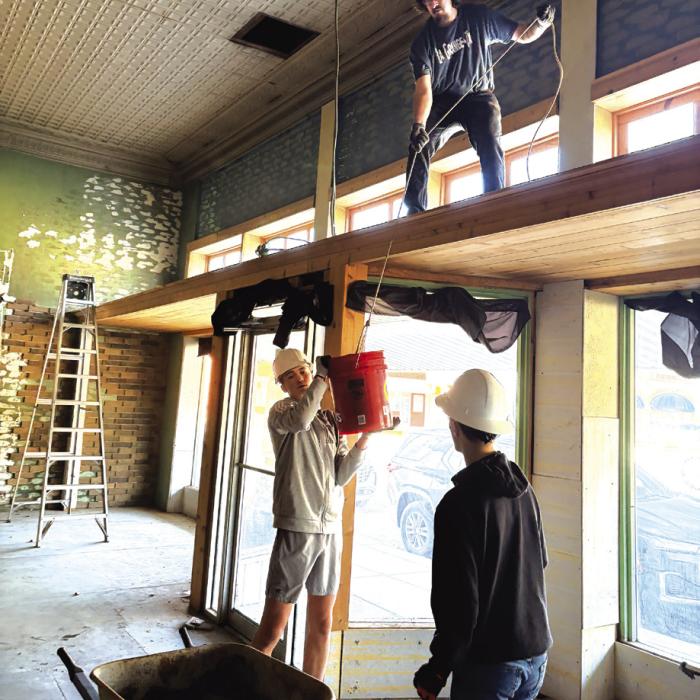 Garrett Reavis, up top, lowers down a bucket of old brick paneling to Deacon Wick and Jude Lira Saturday. All are Fayette Community Theatre volunteers who showed up Saturday to help with initial demolition work at the old Prause’s Meat Market, which will be a new theatre. Photos by Chrystal Wick