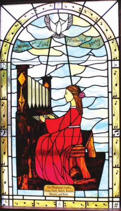 This stained glass window near the pipe organ in Fayetteville, donated by the Pflughaupt family, shows Saint Cecelia (the patron saint of music) playing a pipe organ.