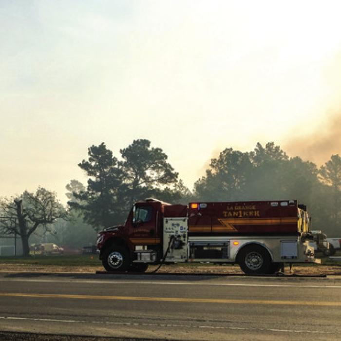 A La Grange fire tanker staged along US 77 near Camp Lost Pines as a plume of smoke from the Whirling Pines Fire rises in the air behind it. Photo by Andy Behlen