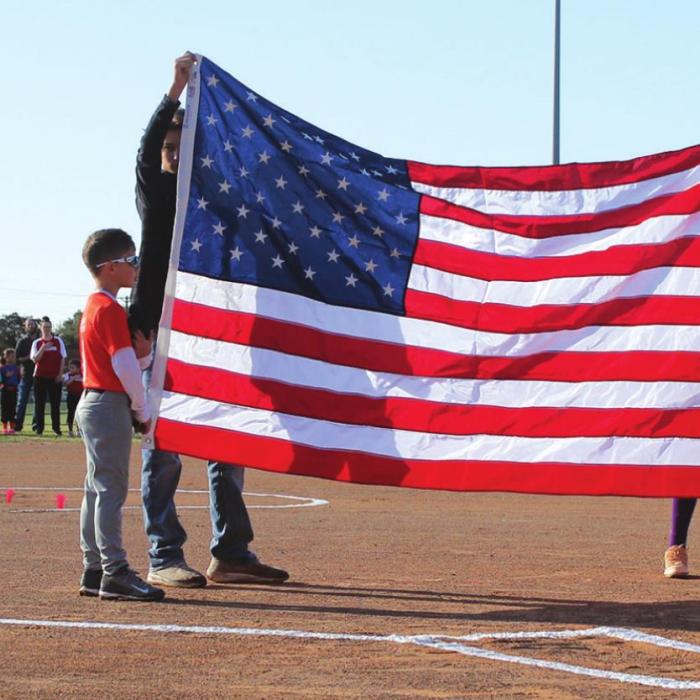 Little Leaguers hold up the flag (with a little help) during the Opening Day ceremony Saturday at the fairgrounds softball fields. Woodmen of the World donated the flag. Behind them stands some of the teams that were announced during the ceremony. Photos by Jeff Wick