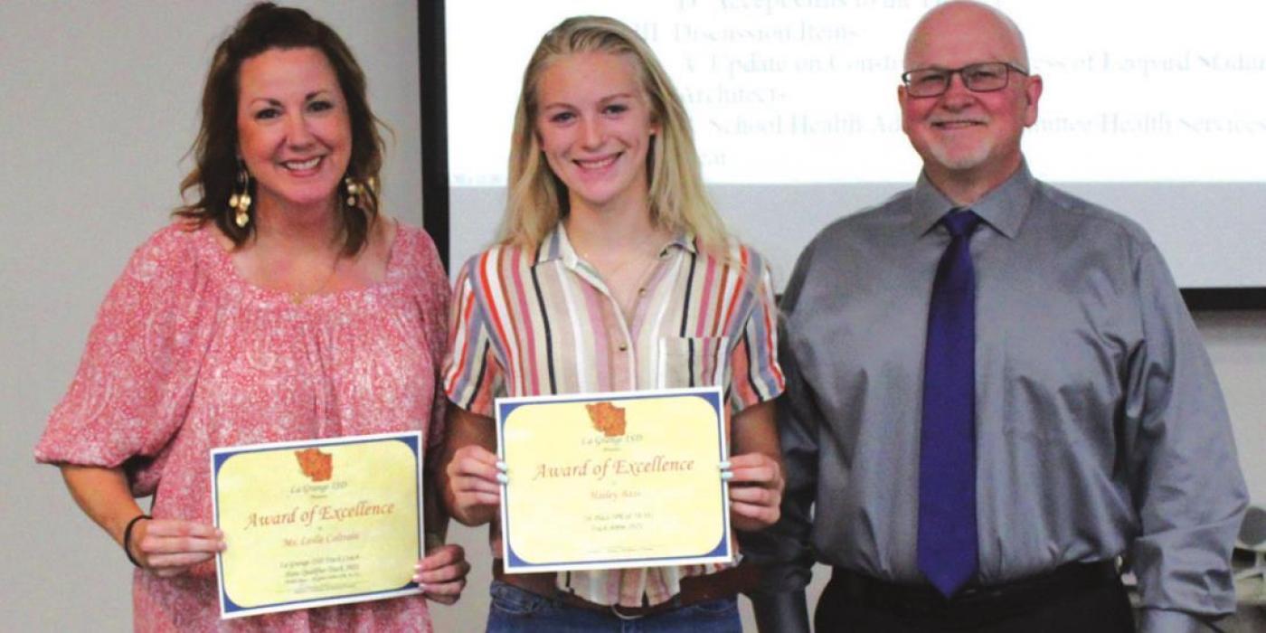Board president Gary Drab presented Hailey Bass, center, an Award of Excellence for advancing to the state track meet. Her coach, Leslie Coltrain, left, was also presented an Award of Excellence.