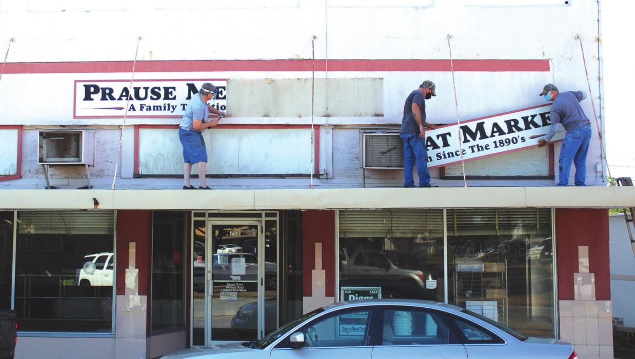 From left to right, Brian, Mark and Gary Prause take down the exterior sign above Prause Meat Market Monday as they prepare to sell the historic building which has housed the market since 1953. The first Prause Market opened on the square in 1904. Photo by Jeff Wick