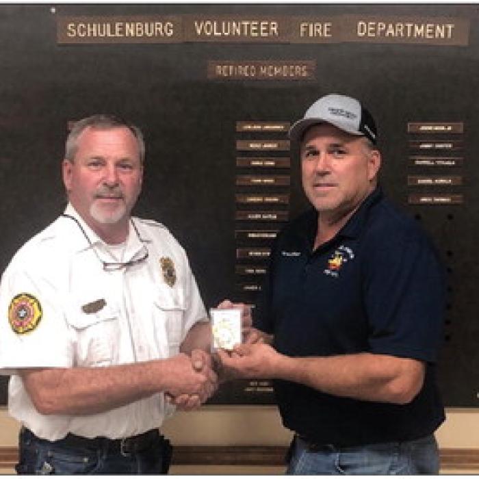 Outgoing Schulenburg Fire Chief Jeff Proske (left) presents the chief’s badge to newly elected Fire Chief Darren Guentert at the department’s meeting last Thursday, Sept. 14.