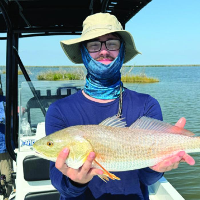 My son, Sam, holds a redfish he caught with my dad and I standing on the side of the boat.