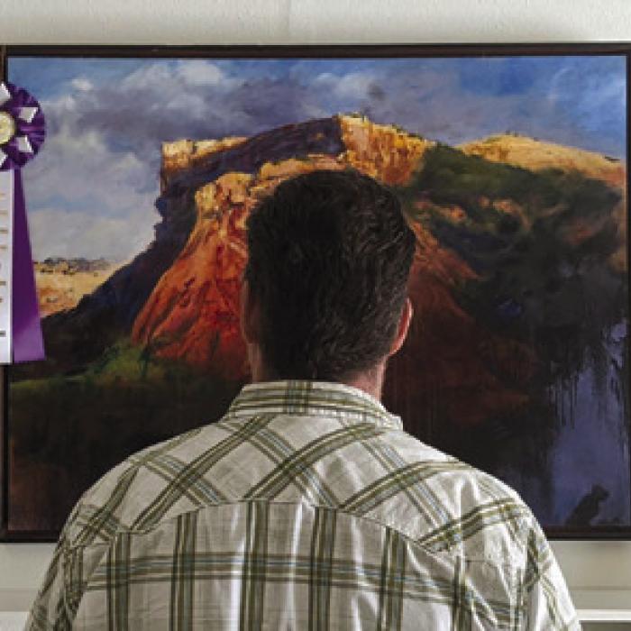 A gallery-goer enjoys Stephen Henry’s oil painting titled “Sunrise on Caprock.”