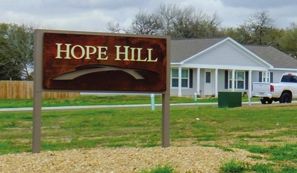 The welcome sign to Hope Hill stands along Horton St., where 20 homes have been built, like the one behind the sign, but 41 empty lots remain. Photo by Andy Behlen