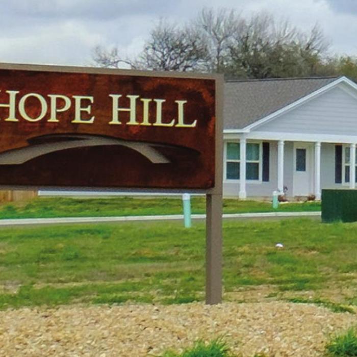 The welcome sign to Hope Hill stands along Horton St., where 20 homes have been built, like the one behind the sign, but 41 empty lots remain. Photo by Andy Behlen