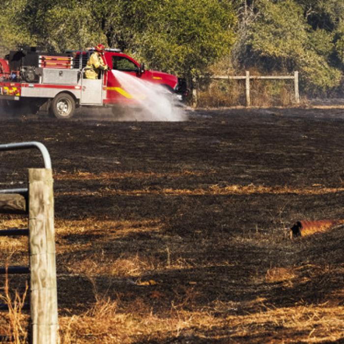 A La Grange fire truck sprays water on smouldering hot spots at a grass fire north of La Grange Friday. Photo by Andy Behlen