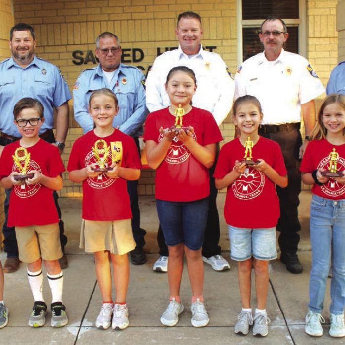 3rd and 4th grades – Left to right, Winners: Blake Markwardt, Cole Hodges, Maggie Kleiber; Honorable Mention: Zaylee Gilbreath, Bailey Tousek, Ava Wied. La Grange firefighters Chris Kaspar, Kenneth Chovanec, Todd Johnson, Glen Knigge, and Blythe Vitek. Photo by Jeff Wick