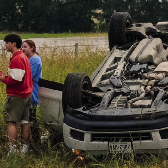 First responders speak to the driver and passenger of a Cadillac SUV that rolled over on SH 71 near Plum on Thursday. No one was seriously injured. Photo by Andy Behlen