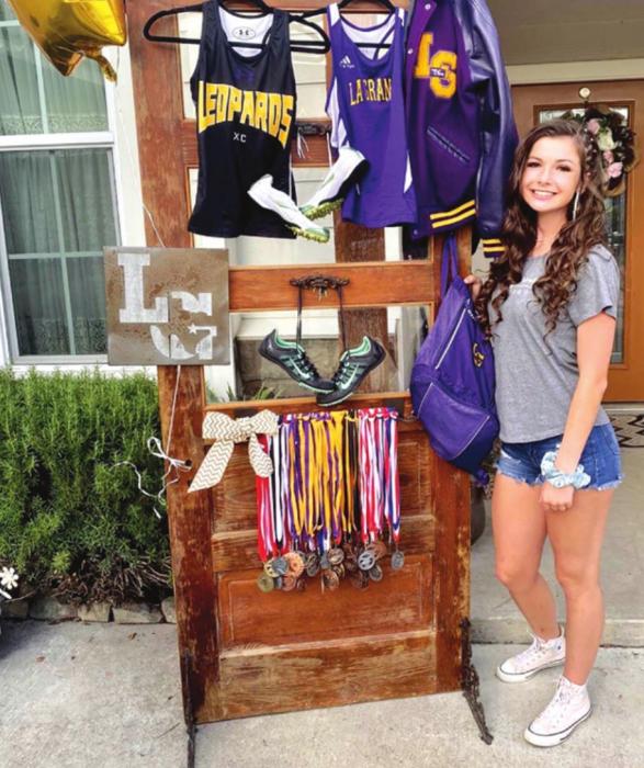 Brenna Iannelli is shown standing alongside the various jerseys she wore and the medals she won as a La Grange athlete. 