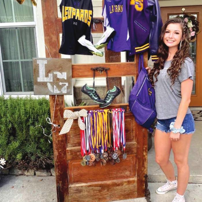 Brenna Iannelli is shown standing alongside the various jerseys she wore and the medals she won as a La Grange athlete. 